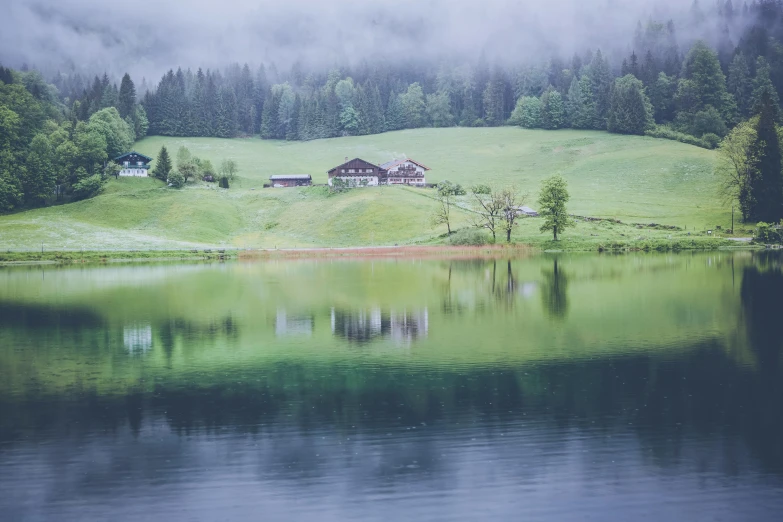 a house is shown on a green hill next to the lake