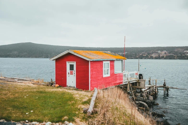 a small red house near the water on a cloudy day