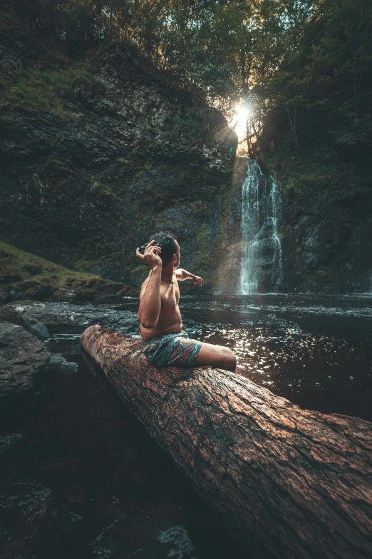 a woman sitting on a log in front of a waterfall
