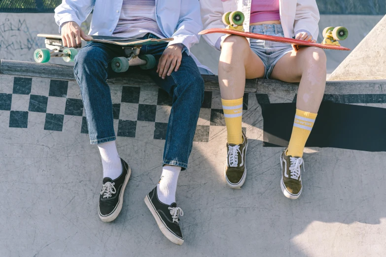 two s, one holding a skateboard, are sitting on the edge of a ramp