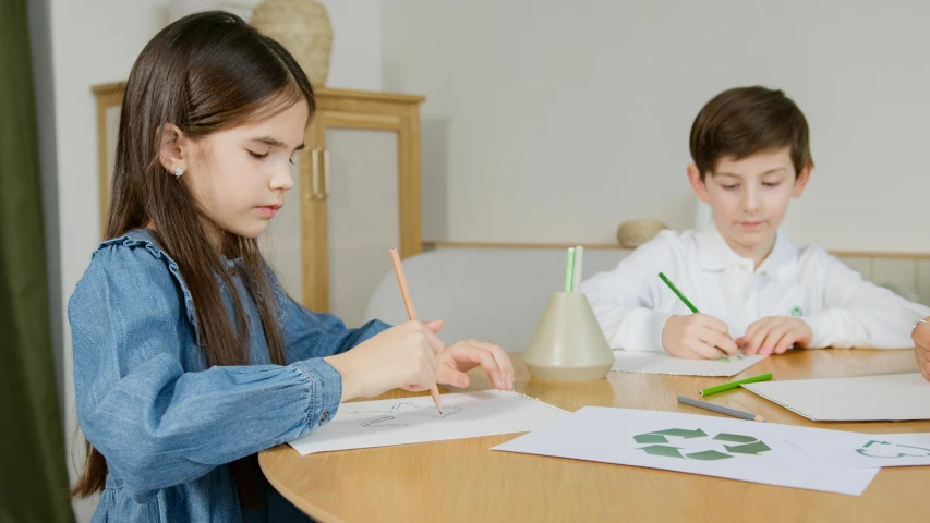 two young children sitting at a table doing arts and crafts