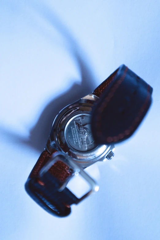 a silver watch on a white surface with a brown strap