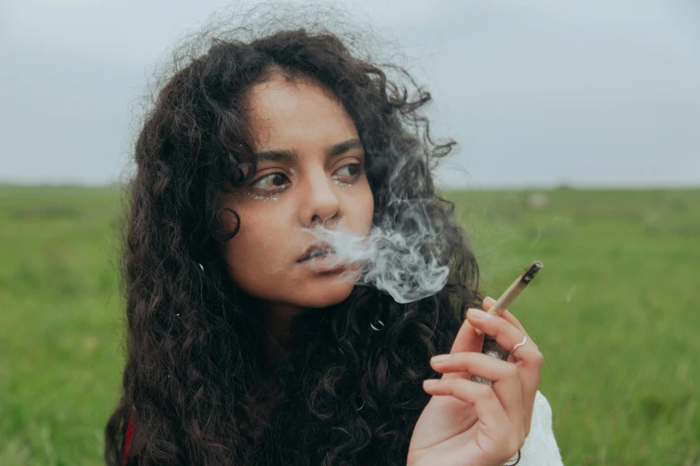 a woman in a grassy field smokes a cigarette