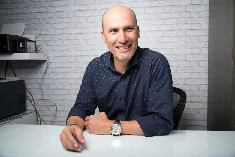 the man smiles at the camera while seated in front of his computer