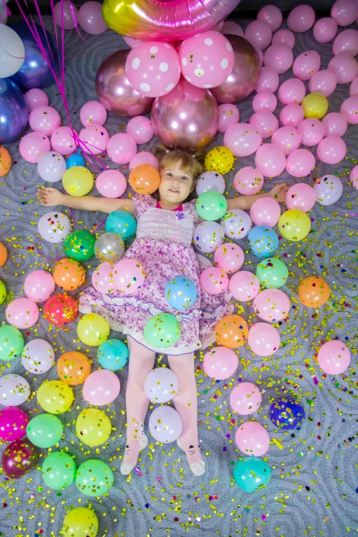 girl laying in balloons that are falling off
