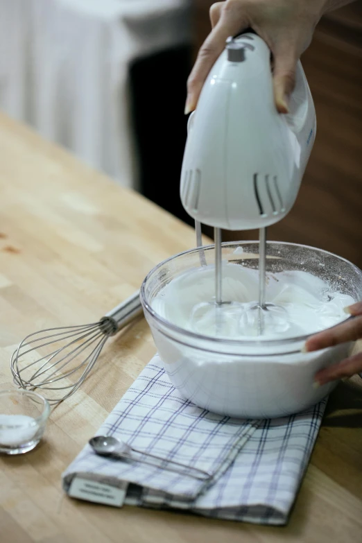 a person mixing cream inside of a bowl on top of a table