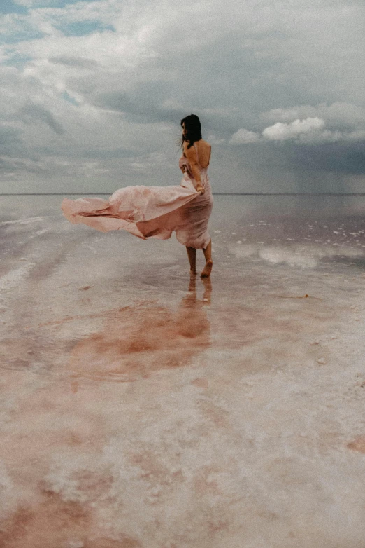 the woman is standing on the beach in front of a cloudy sky