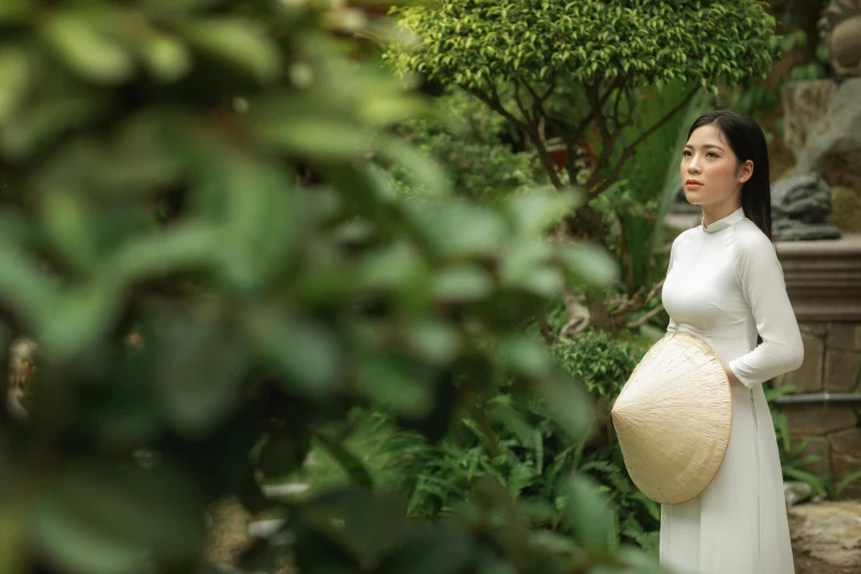 a young lady wearing a white dress and hat in an oriental garden