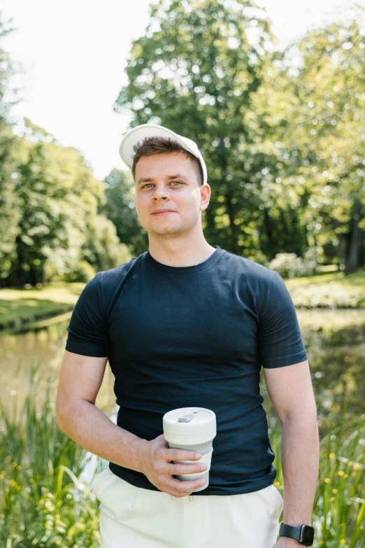 man holding a coffee cup standing near pond with water