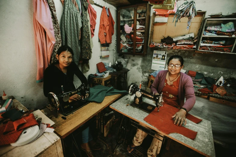 two women work in an old, dusty room with many sewing supplies on shelving shelves