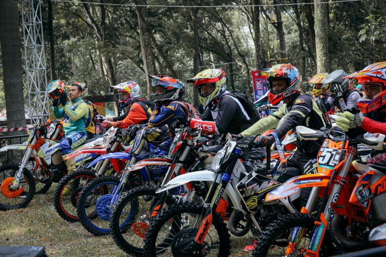 several people in red helmets are standing around their dirt bikes