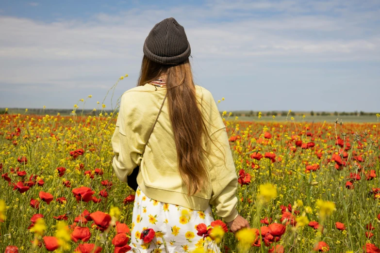 girl with hat standing in an open field of poppies