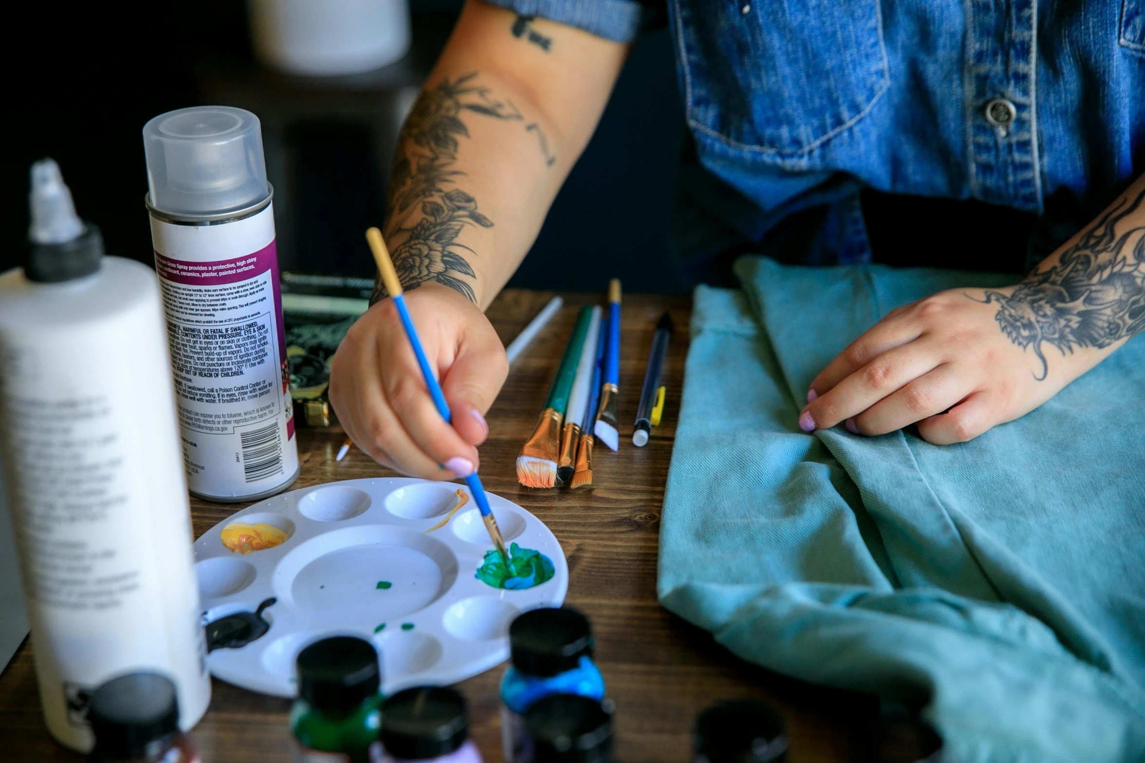 a tattooed woman's hands painting on an easel with paint