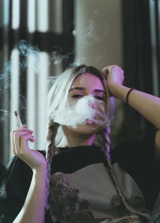 a woman with white smoke in her mouth, and a id on her head, holds a cigarette in her hand