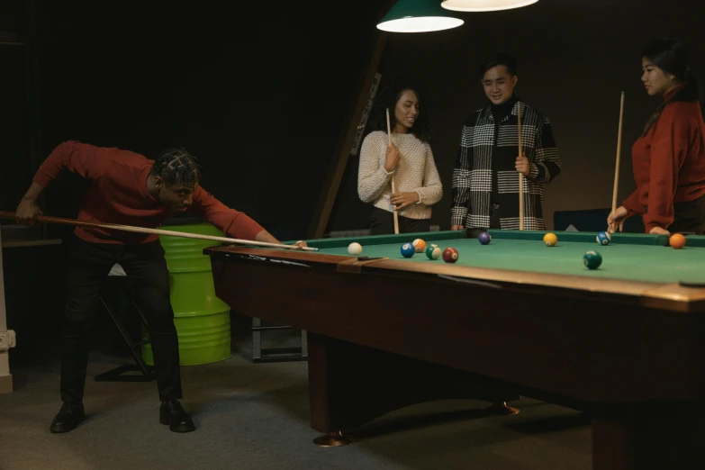 three women and two men are playing a game of pool