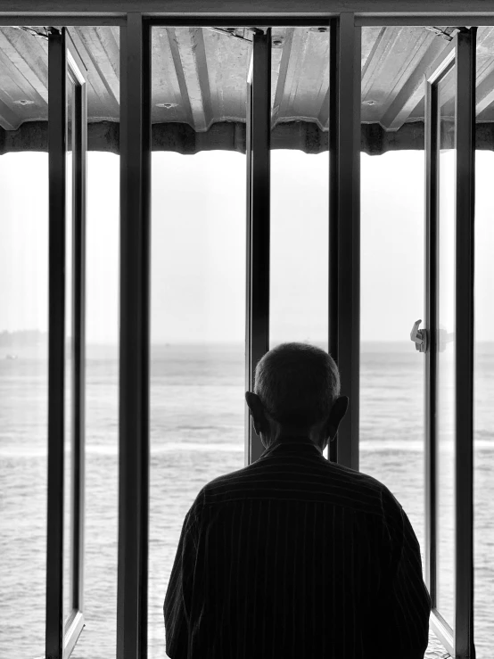 a man in black and white sitting outside a window looking out on the water