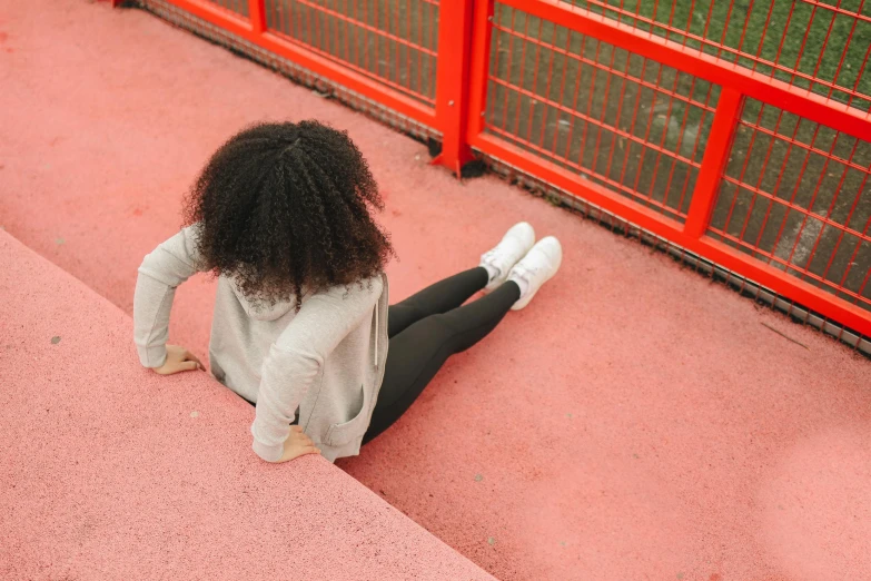 a little girl sitting on the ground by a fence