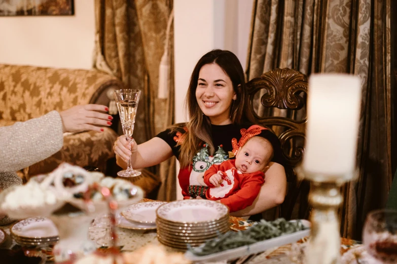 two woman sit at a table holding a baby while holding a champagne glass