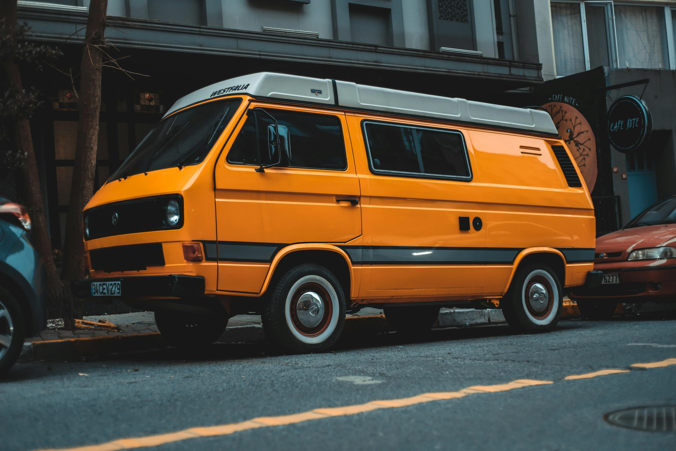 an orange van sitting on the side of a road near parked cars