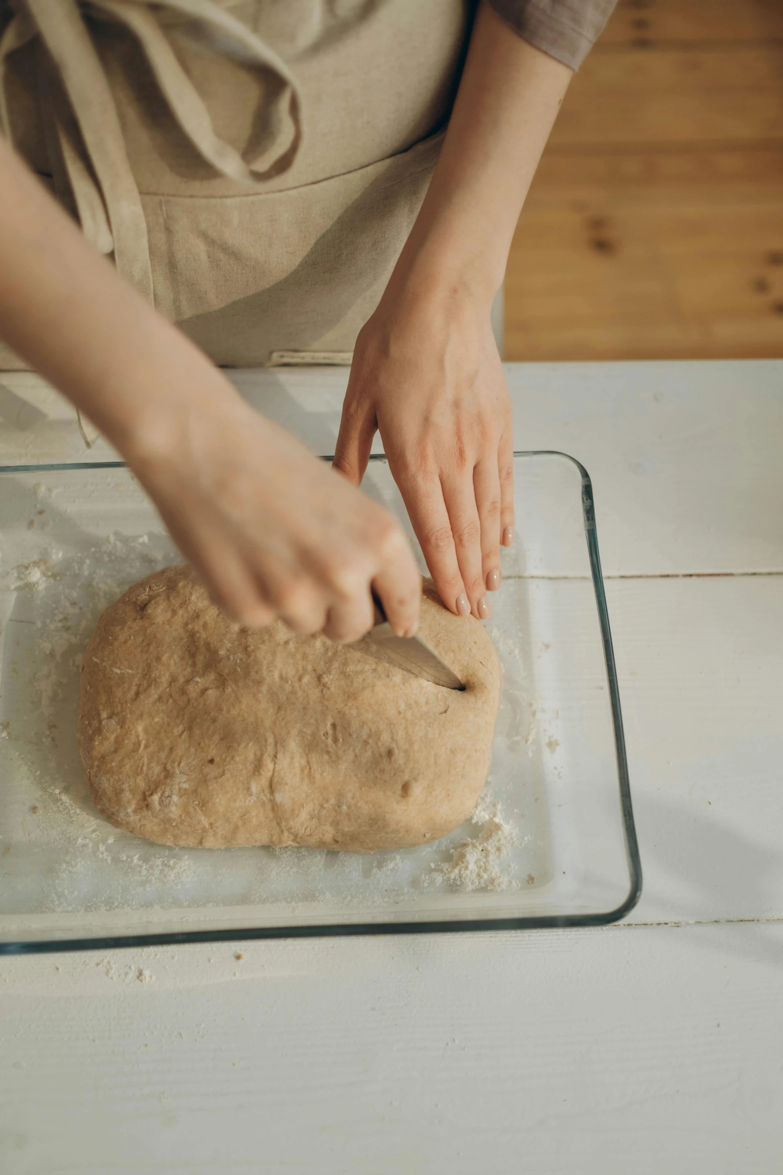 a person in apron using a knife to cut up bread