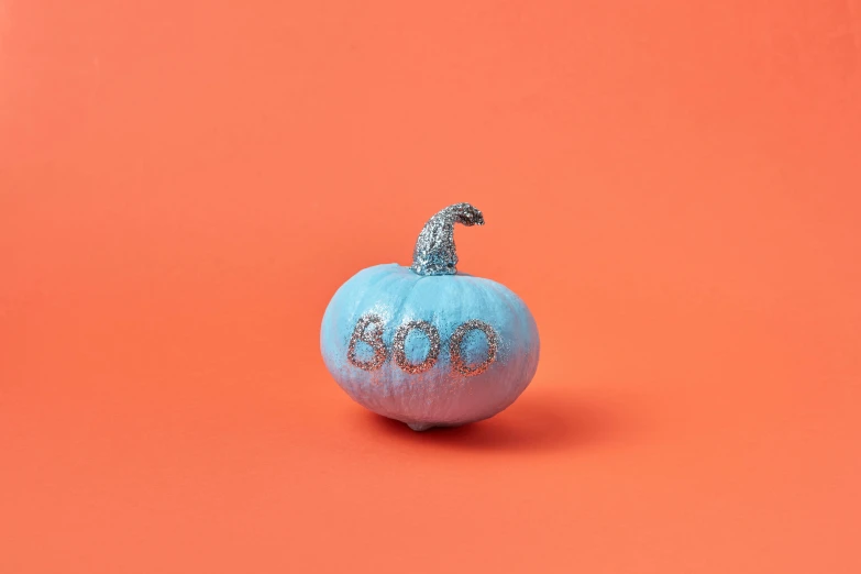small pumpkin with glitter in the letters bleu sitting on a pink surface
