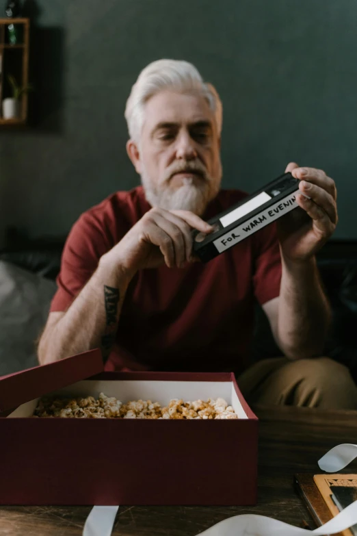 a man in red shirt sitting on a couch and holding up a box with some popcorn