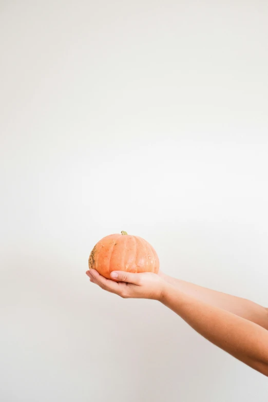 someone holding an orange up against a white wall