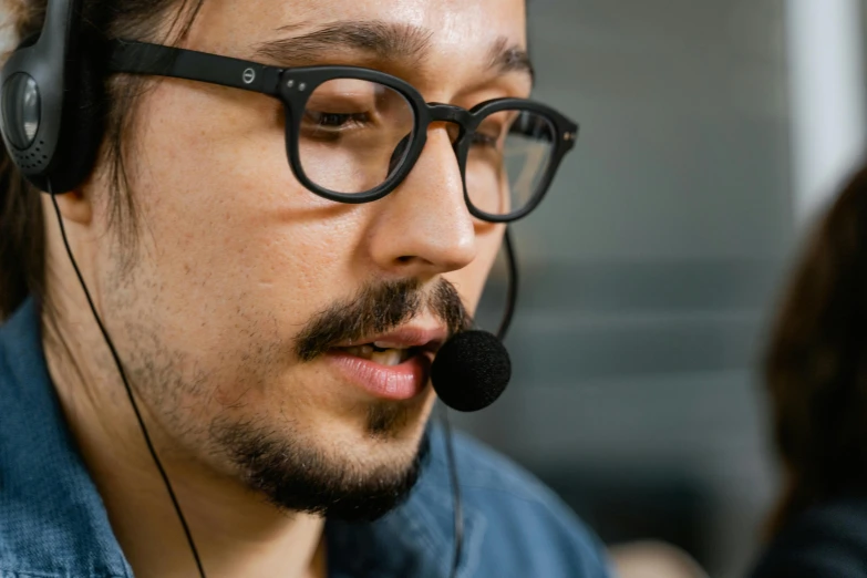 man wearing glasses, a on up shirt and headphones looking at soing on his laptop