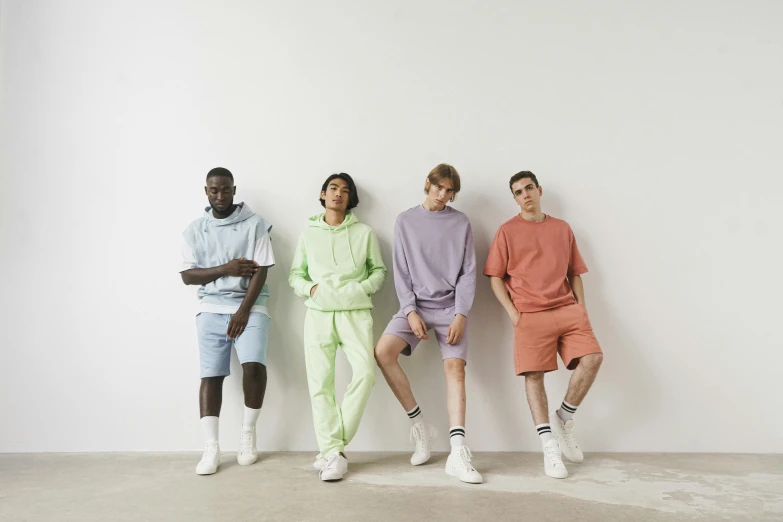 four young men sitting against the wall wearing paste clothing