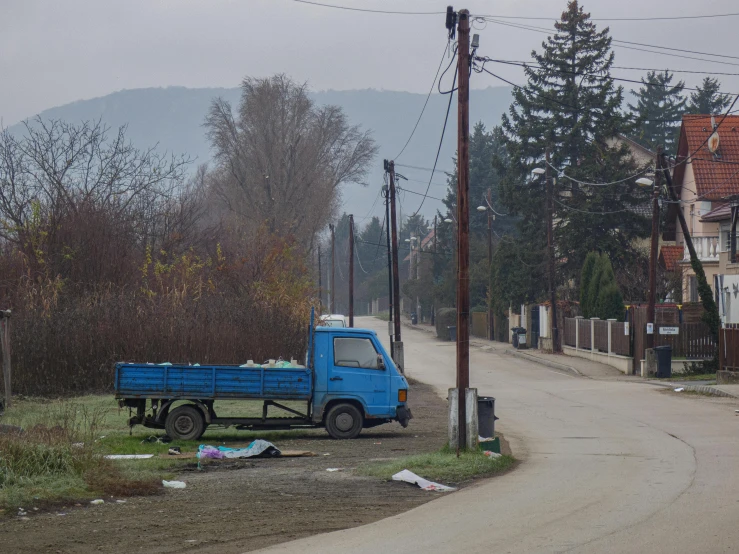 a small blue pickup truck parked on a dirty street