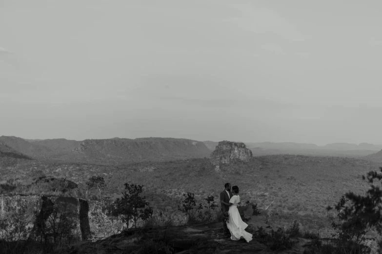 a bride and groom stand on top of a mountain