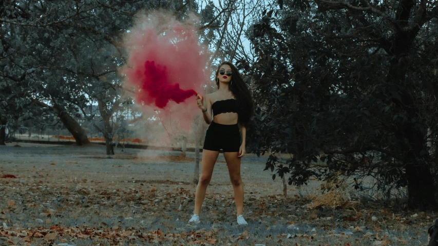 a woman in sunglasses and a bikini holds a red powder in the forest