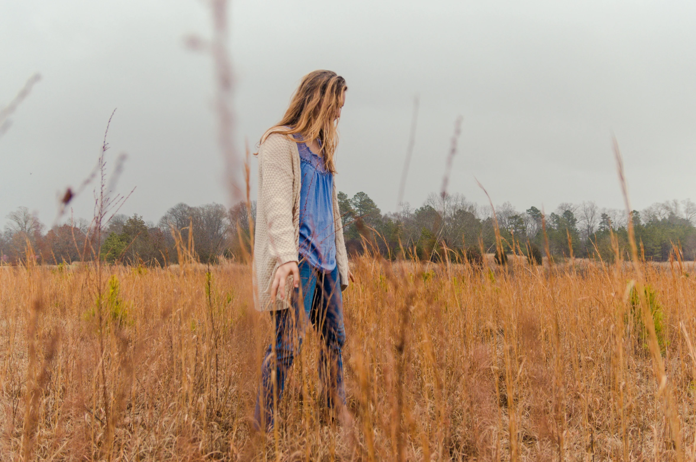 a girl with long hair wearing a sweater in an open field