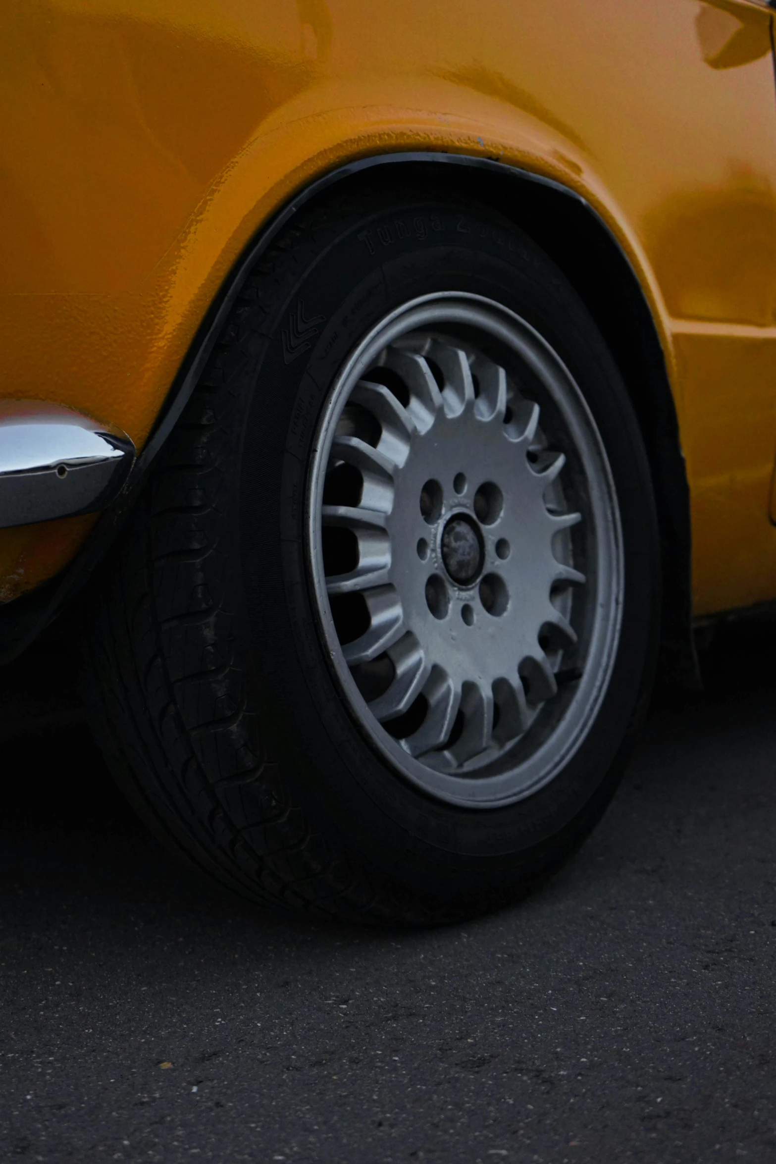 a yellow car with some white spokes is on the pavement