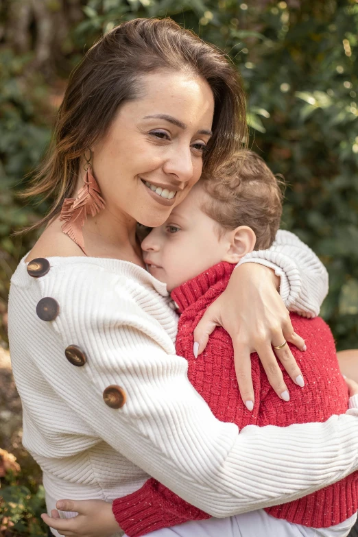 a woman hugging a child while standing in front of some trees