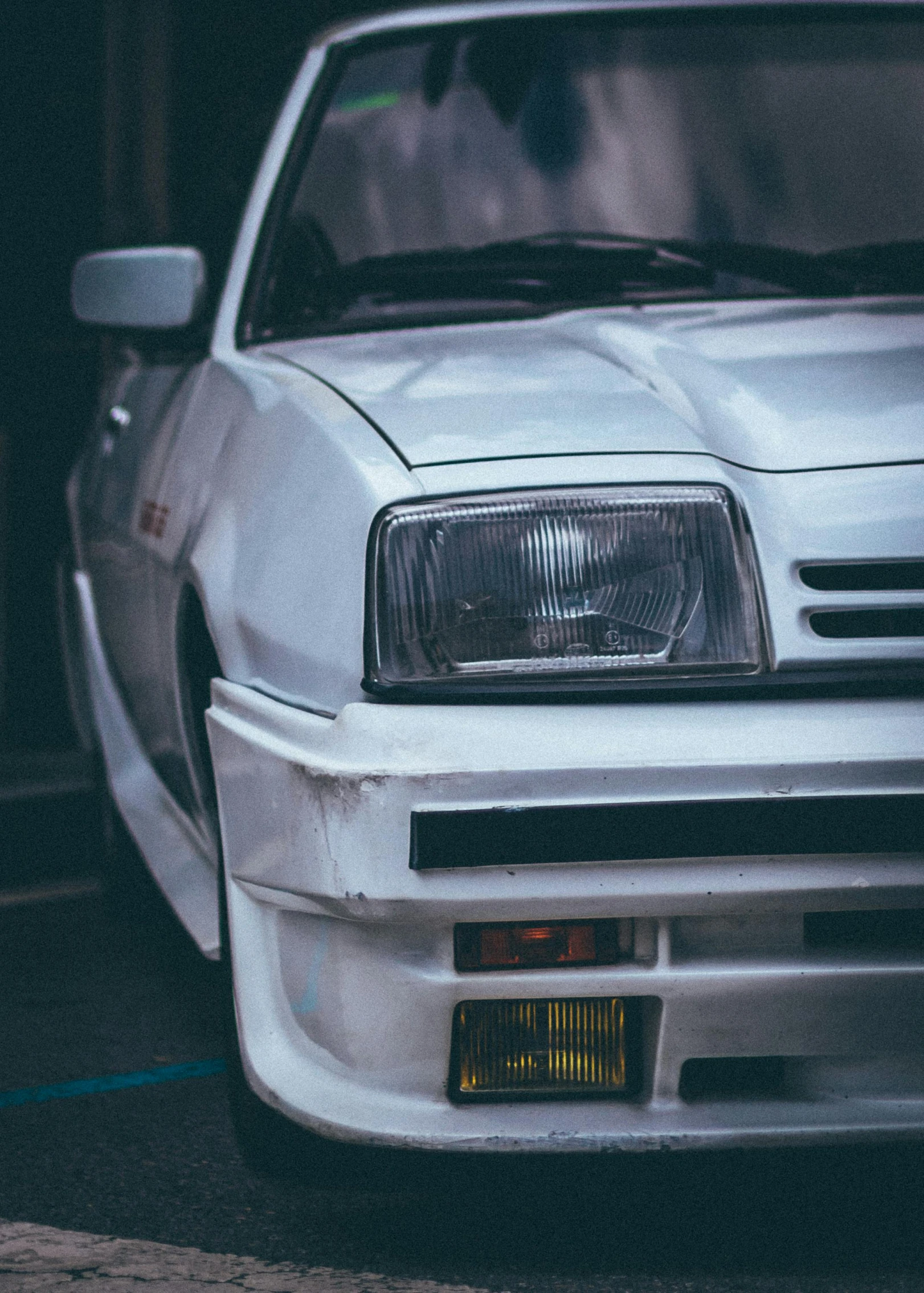 the front end of a white car parked on a street