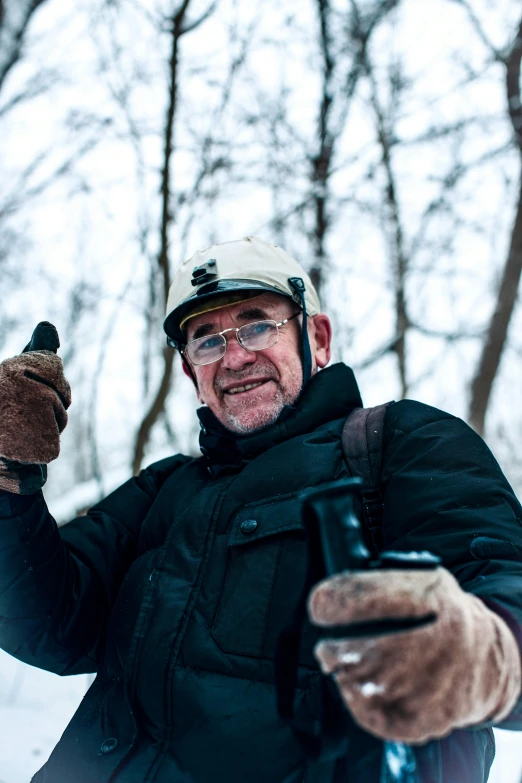 an older gentleman wearing glasses and holding a cellular phone in a winter setting