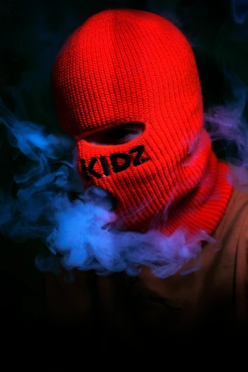 a person wearing a red knitted hat with the words z on it in a fog covered black background
