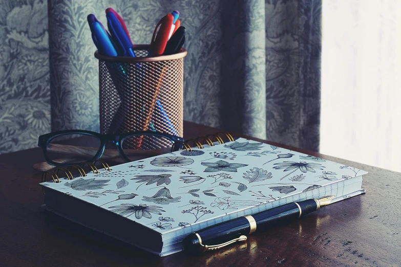 an opened notebook with pens and glasses on top