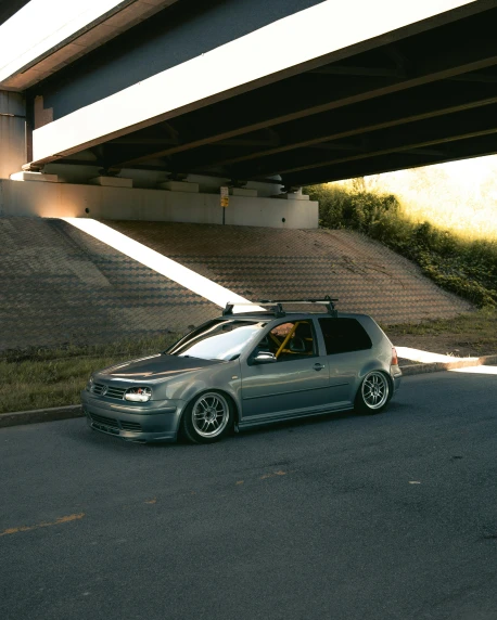 a small grey car on a road under an overpass