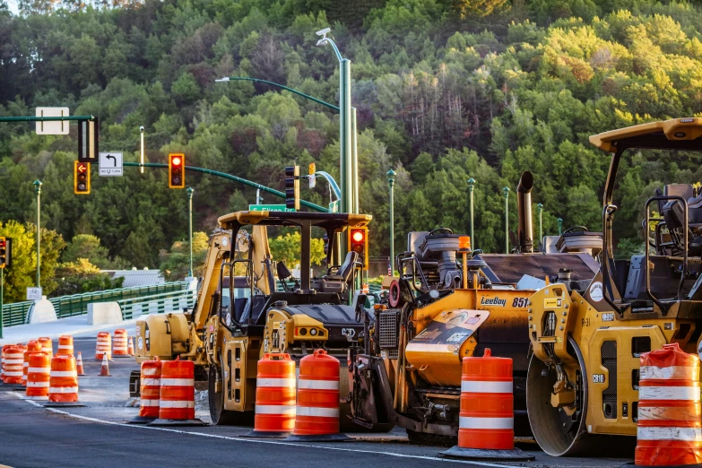 three yellow road construction vehicles sitting in front of road work cones
