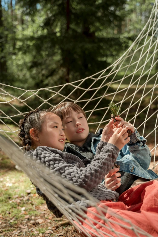 two children with a small plant sitting in a hammock