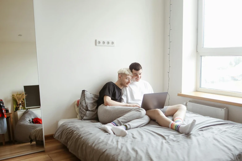 the man and woman are sitting on the bed looking at their laptop