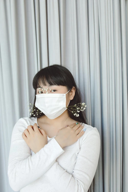 woman wearing white face mask against a curtain