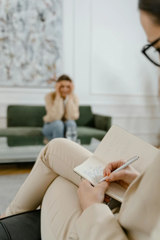 a woman sitting on a couch holding a cellphone and writing in her hand