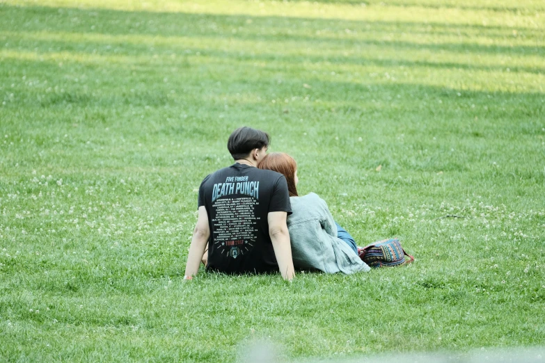 a couple is sitting in the grass, one has his back to the other