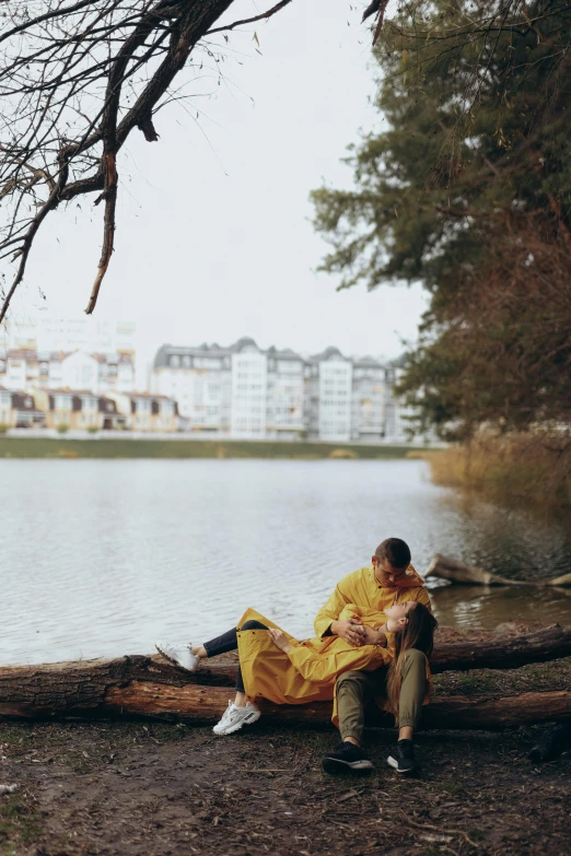 a couple sitting on a log next to a lake