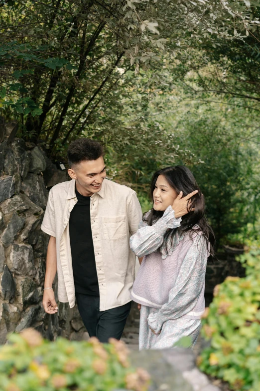 young couple smiling into each others eyes as they walk by rock wall and trees
