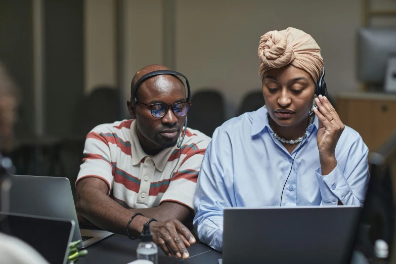 two people sitting around a laptop, one using a phone