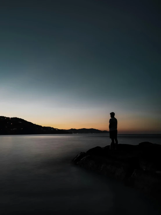 a man standing on a rock near the ocean watching the sun set